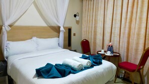 Une chambre d’hôtel avec un lit, une table de chevet, une table avec une chaise et un rideau.
