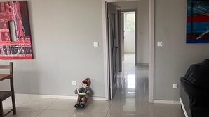 A spacious living room with a tiled floor, a wooden chair, a black sofa, and a small toy figure. - Modern apartment with incredible views (Le Crès)