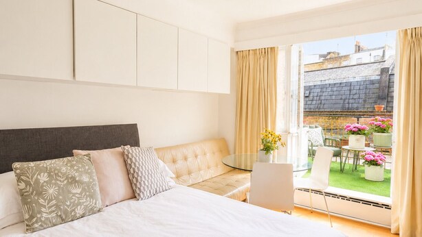 A bedroom with a bed, a sofa, a laptop, and a view of the outside. - Terraced studio, Baker street (London)