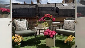 A rooftop patio with two green sofas, a small round table, and potted plants. - Terraced studio, Baker street (London)