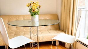 A modern room with a glass table, two white chairs, a beige sofa, and a window with curtains. - Terraced studio, Baker street (London)
