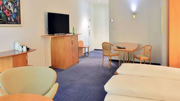 Habitación de hotel con cama, escritorio con televisor, zona de comedor con sillas y un cuadro en la pared.