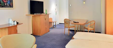 A hotel room with a bed, a desk with a television, a dining area with chairs, and a painting on the wall.