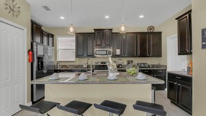 A modern kitchen with dark cabinets, stainless steel appliances, and a central island with bar stools. - Last Minute Disney! Private Pool, Hot Tub & Themed Bedrooms. Book Now! #65723 (Orlando)