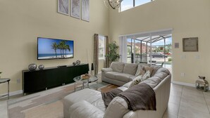A spacious living room with a large window, a flat-screen TV, a sofa, and a coffee table. - Last Minute Disney! Private Pool, Hot Tub & Themed Bedrooms. Book Now! #65723 (Orlando)
