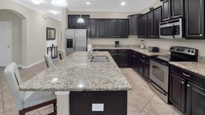 Una cocina moderna con armarios oscuros, encimeras de granito, electrodomésticos de acero inoxidable y una isla central con asientos.