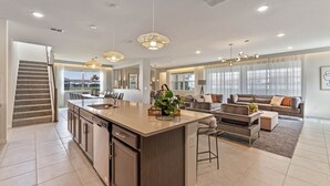 Una cocina amplia con una isla central, un comedor con sofá y sillas, y una escalera que lleva a un nivel superior.