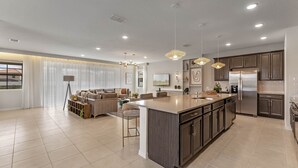Una cocina moderna con una isla grande, electrodomésticos de acero inoxidable e iluminación colgante.