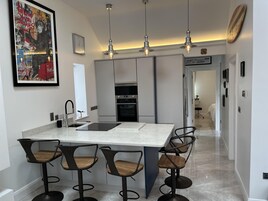 A modern kitchen with a central island, bar stools, pendant lighting, and a large framed artwork.