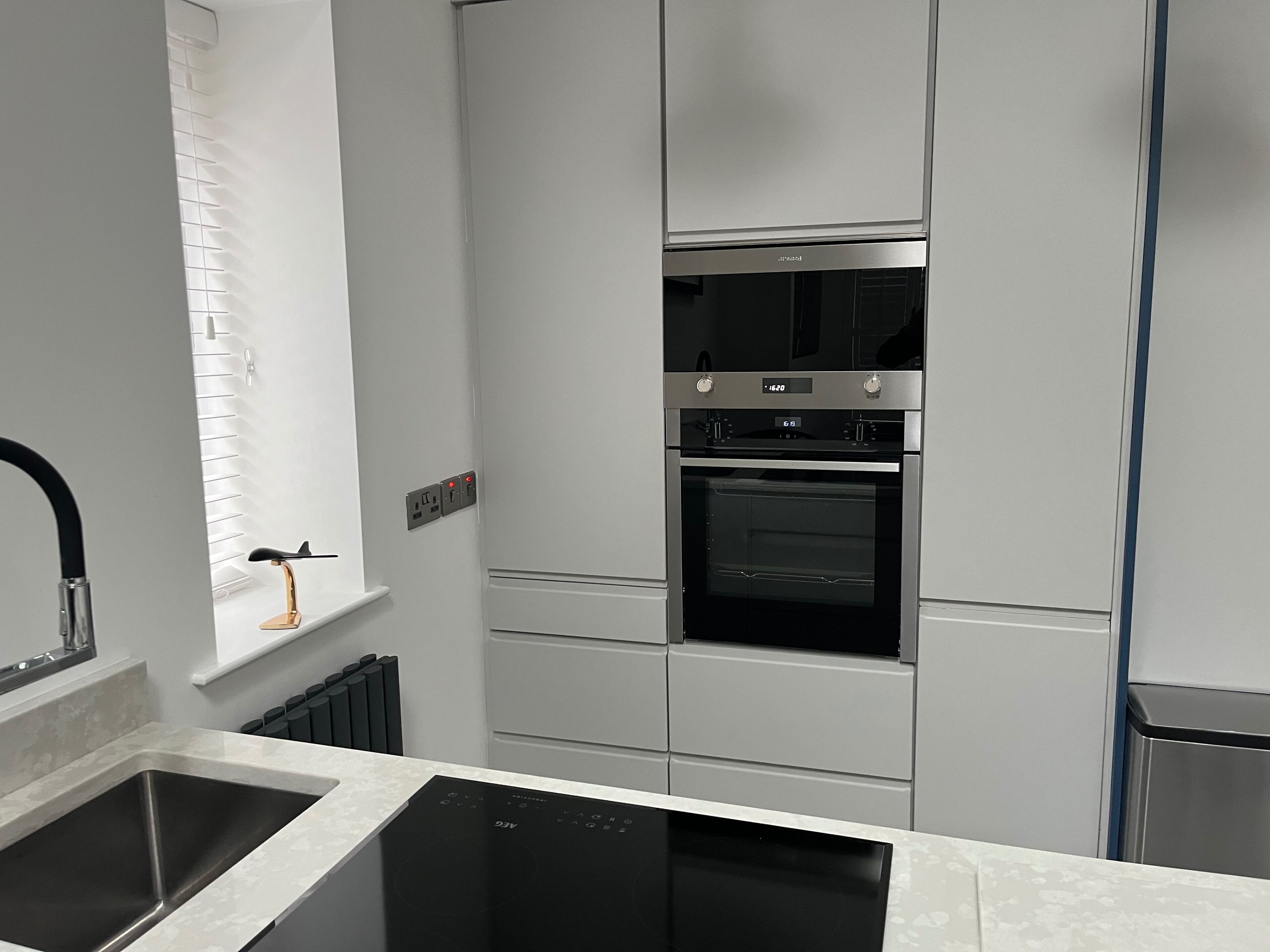 A modern kitchen with a built-in oven, a dishwasher, and a window with blinds.