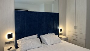 A modern hotel room with a large bed, a nightstand with a remote control, a wardrobe with a mirror, and wall-mounted lighting. - Cottage-sleeps 5-parking-near Beach-fireplace (Buncrana)