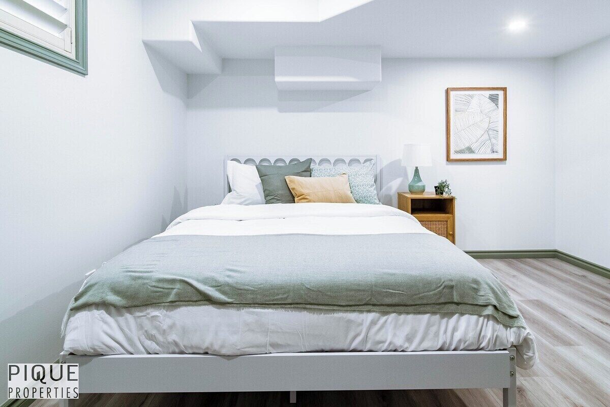 Une chambre à coucher moderne avec un lit, une table de chevet, une lampe et un tableau encadré au mur.