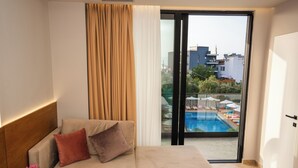 Habitación de hotel moderna con sofá, una pequeña mesa redonda y vista a una piscina a través de un ventanal.