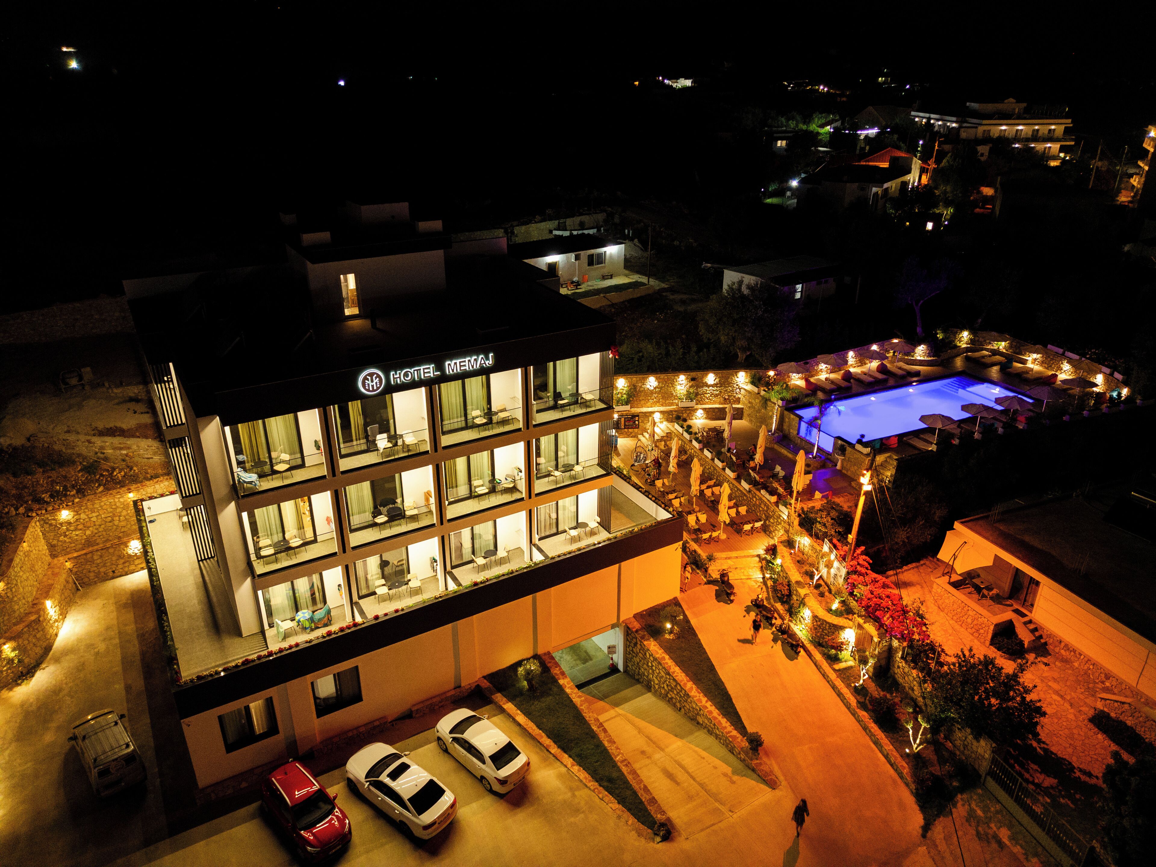 A modern hotel with multiple floors, a swimming pool, and a well-lit outdoor area.