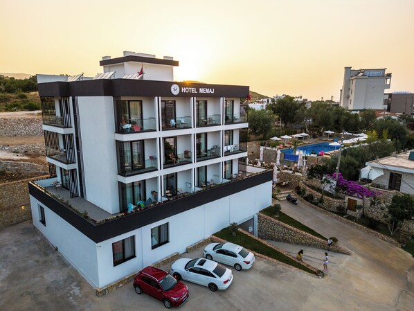 A modern hotel with multiple balconies, a swimming pool, and a parking area.