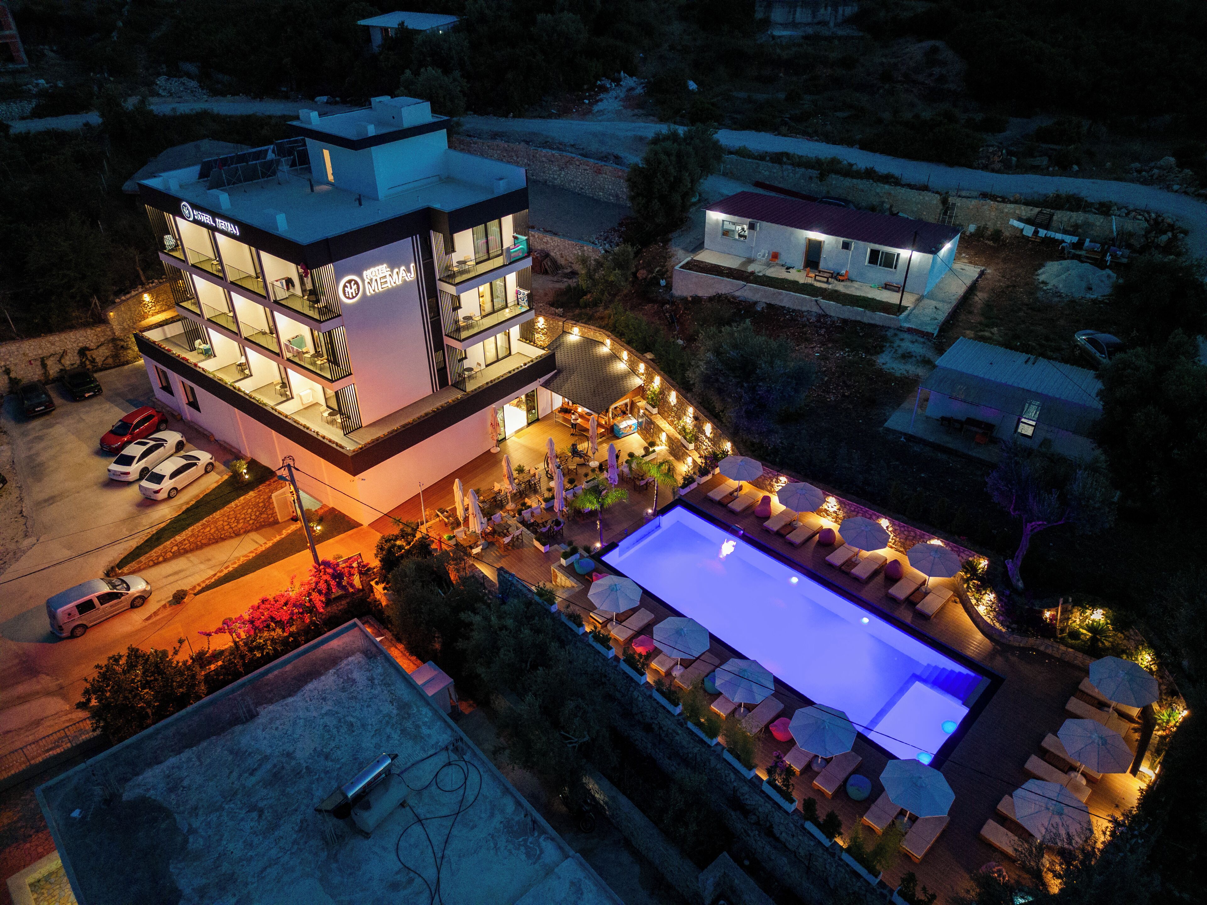 A hotel with a rooftop pool, outdoor seating, and a well-lit entrance.