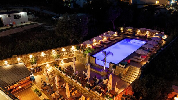 Un área de piscina en la azotea con sillones de descanso y sombrillas, rodeada de muros de piedra y plantas en macetas.