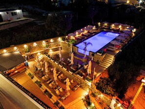 A rooftop pool area with lounge chairs and umbrellas, surrounded by stone walls and potted plants.