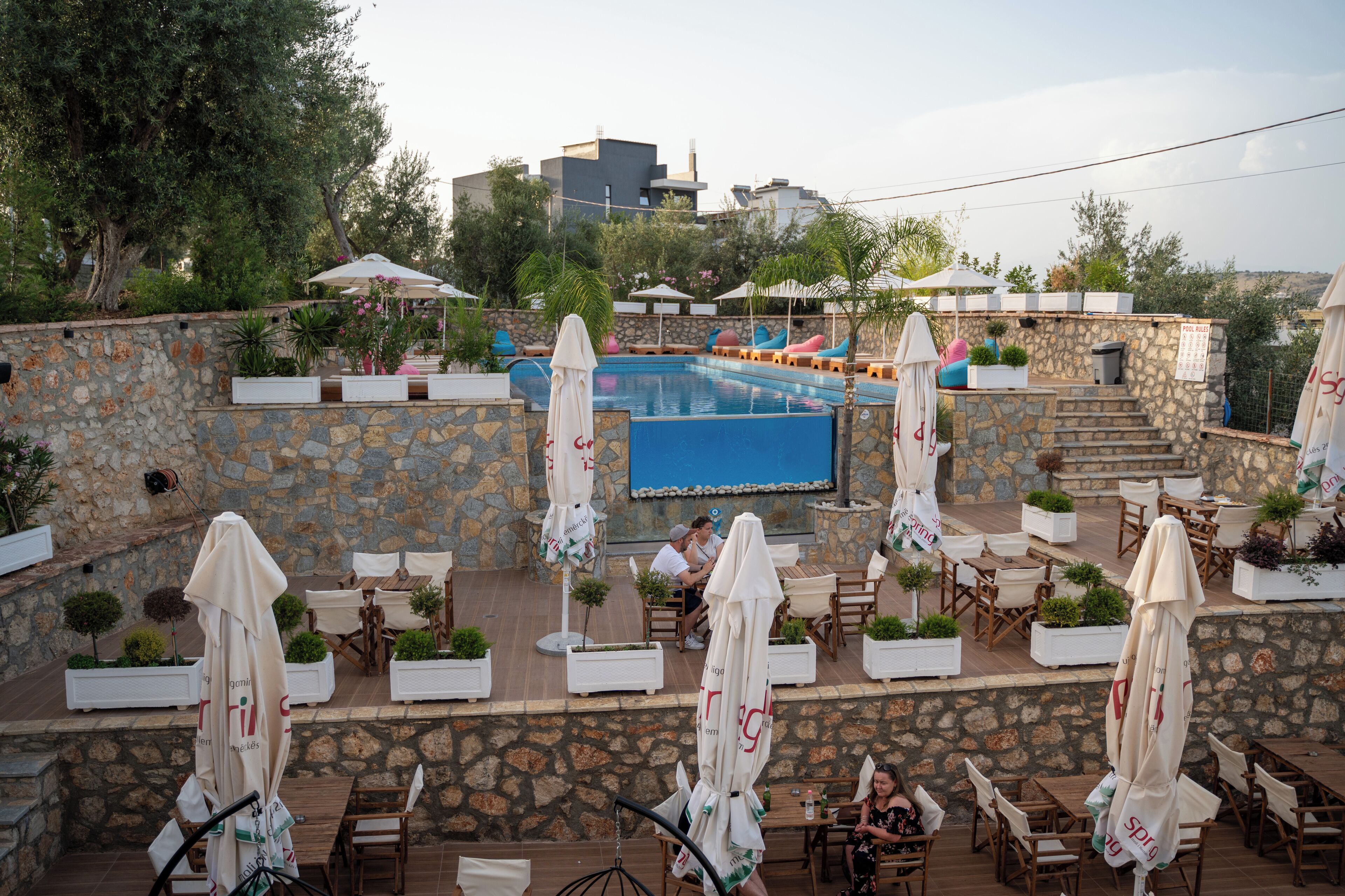 An outdoor pool area with stone walls, lounge chairs, and umbrellas.