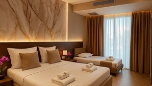 Habitación de hotel con una cama grande, una cama más pequeña y una cama sofá. Hay una pared de mármol y un ventanal con cortinas.