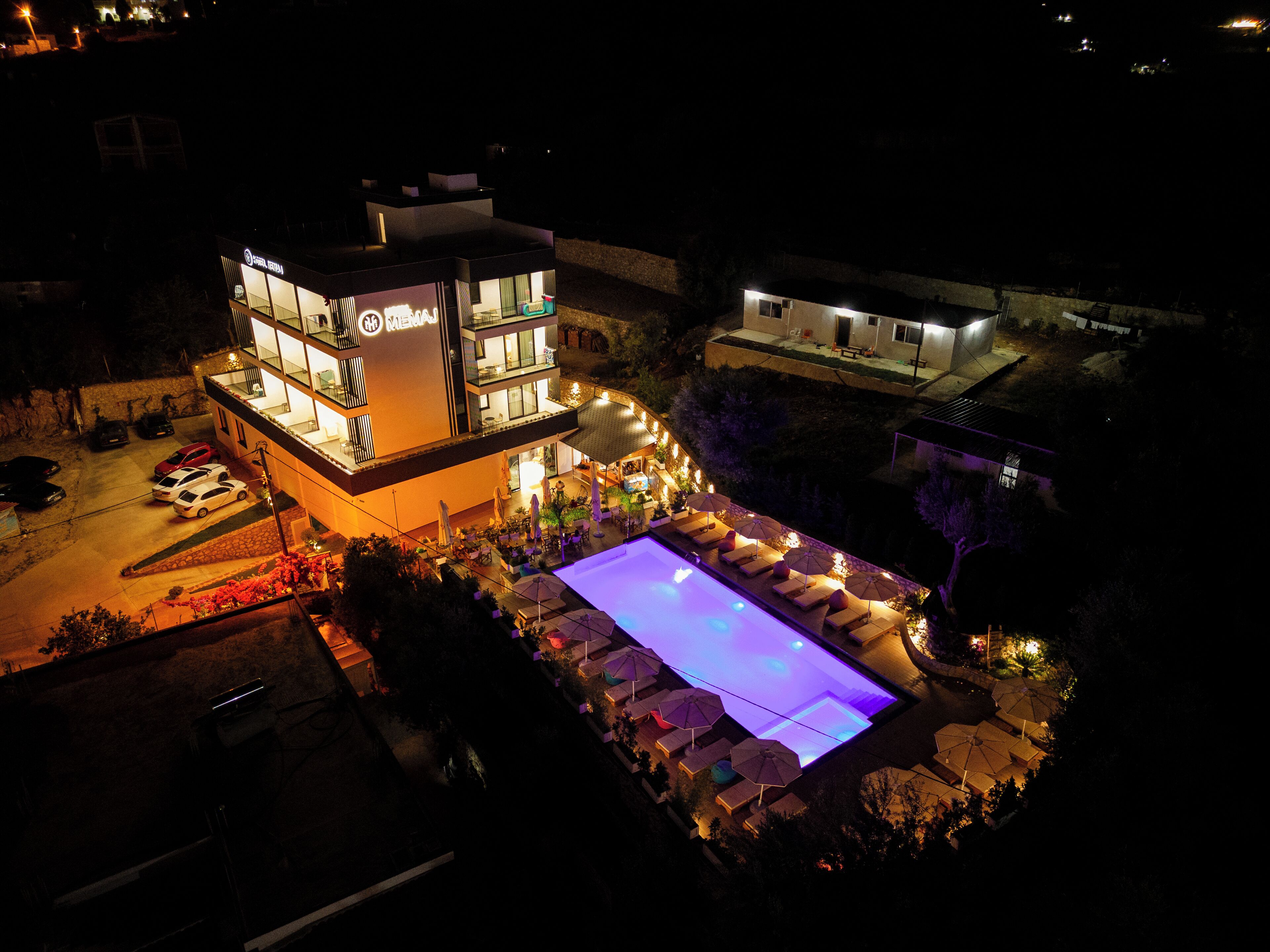A multi-story hotel with a swimming pool, outdoor seating, and a well-lit entrance.