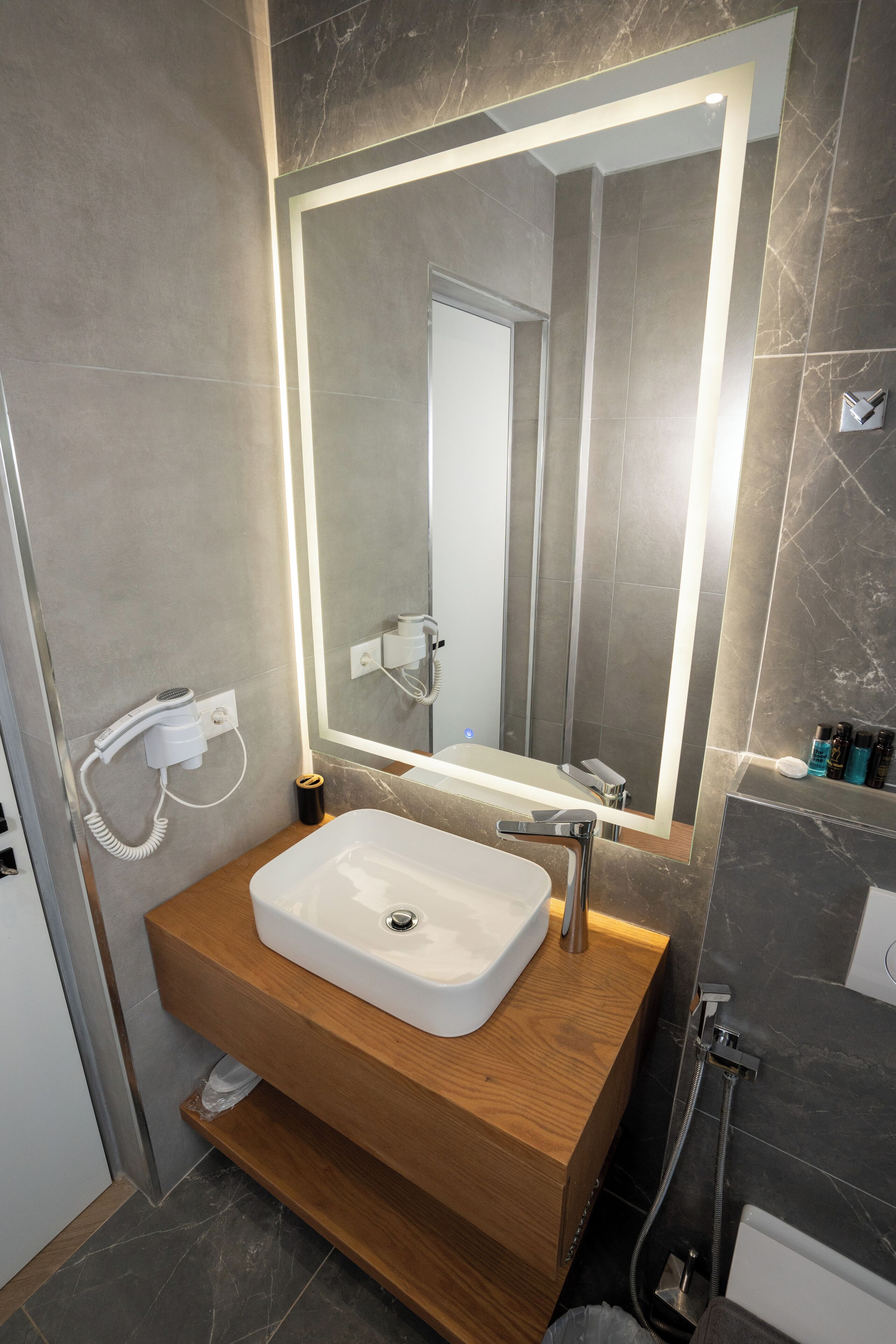 Un bagno moderno con un mobile vanitario in legno, un lavandino bianco, uno specchio grande e una zona doccia.