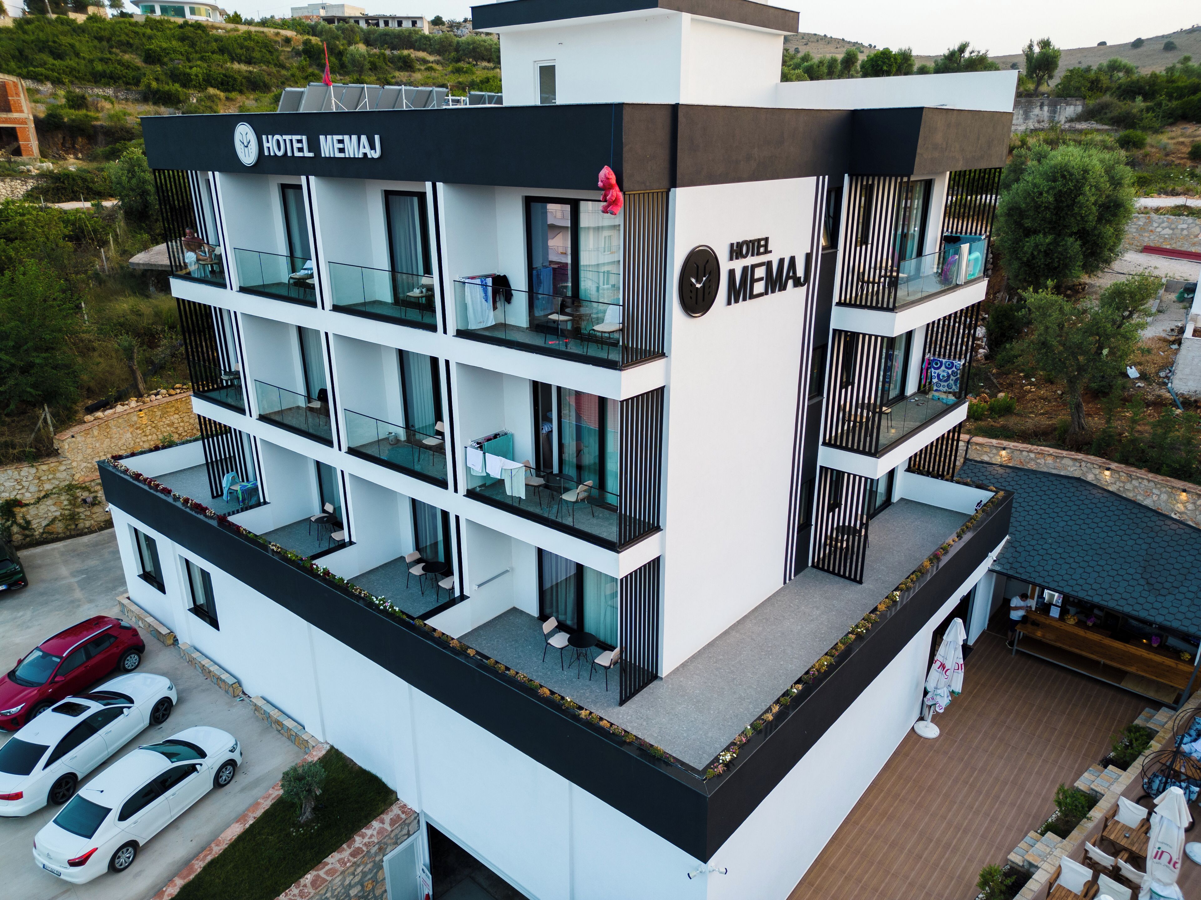 A modern hotel with multiple balconies, a rooftop terrace, and a parking area.