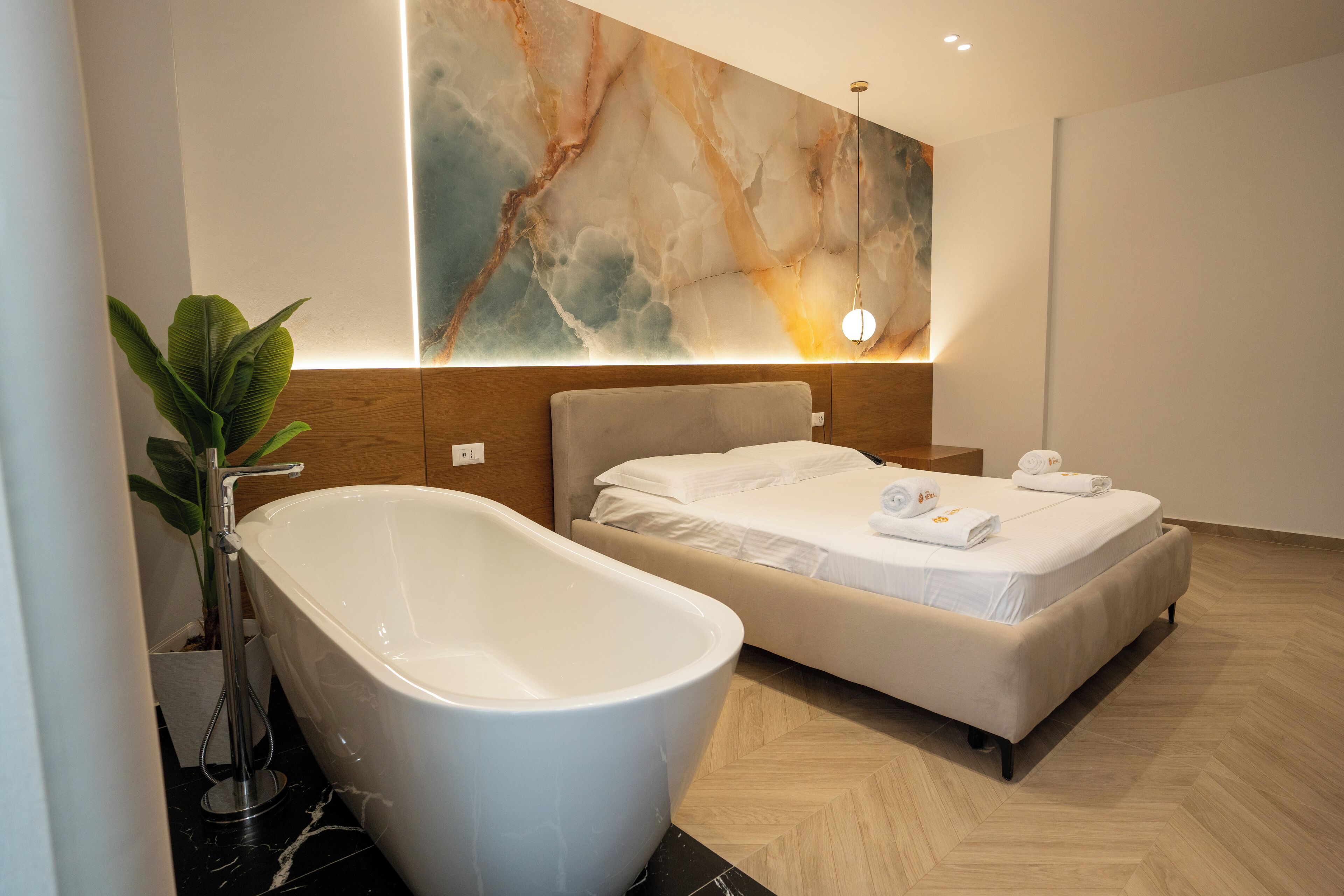 A modern bathroom with a freestanding bathtub, a bed with white linens, and a large abstract wall art piece.