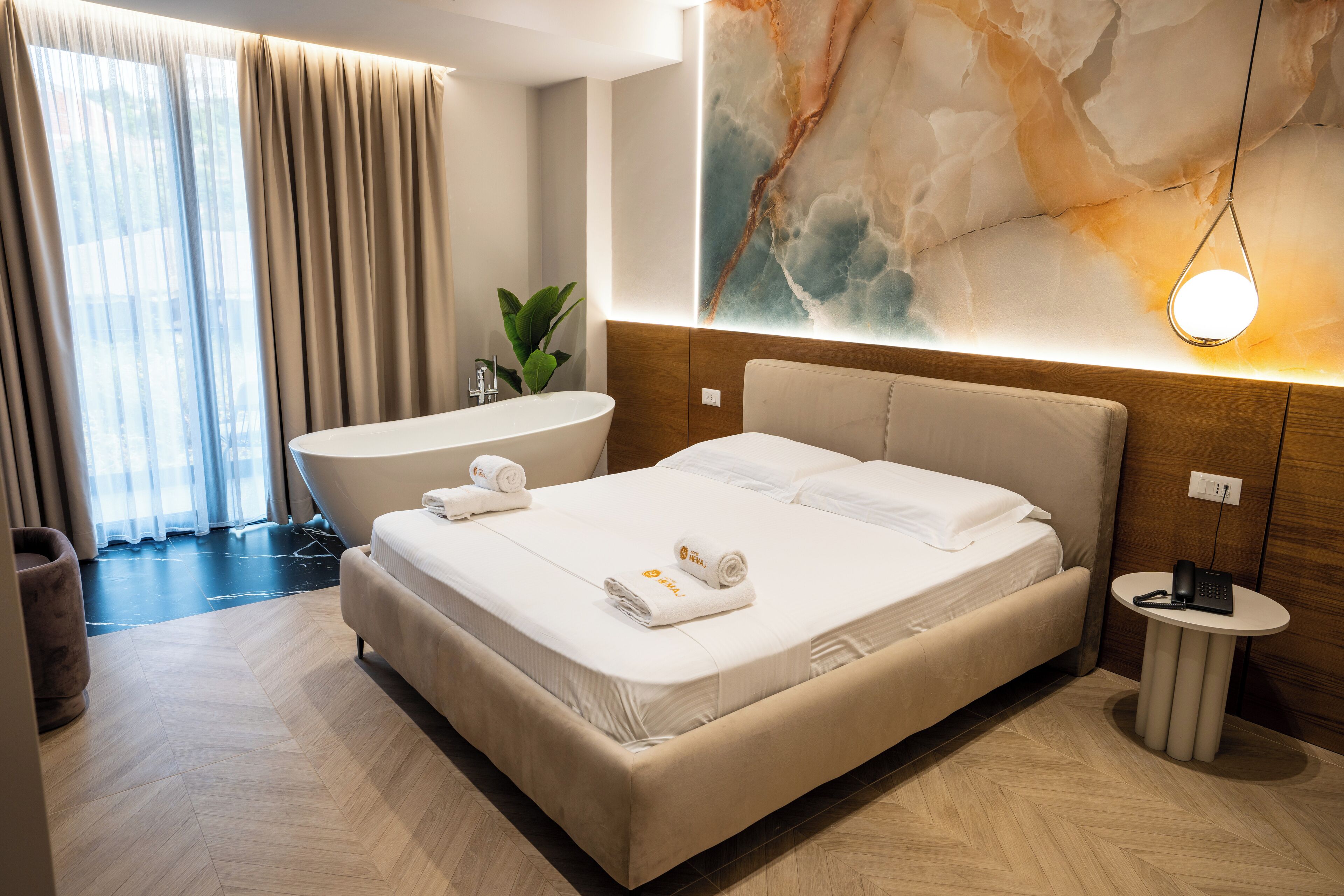 Quarto de hotel moderno com uma cama grande, banheiro privativo, uma mesinha e uma grande obra de arte abstrata na parede.