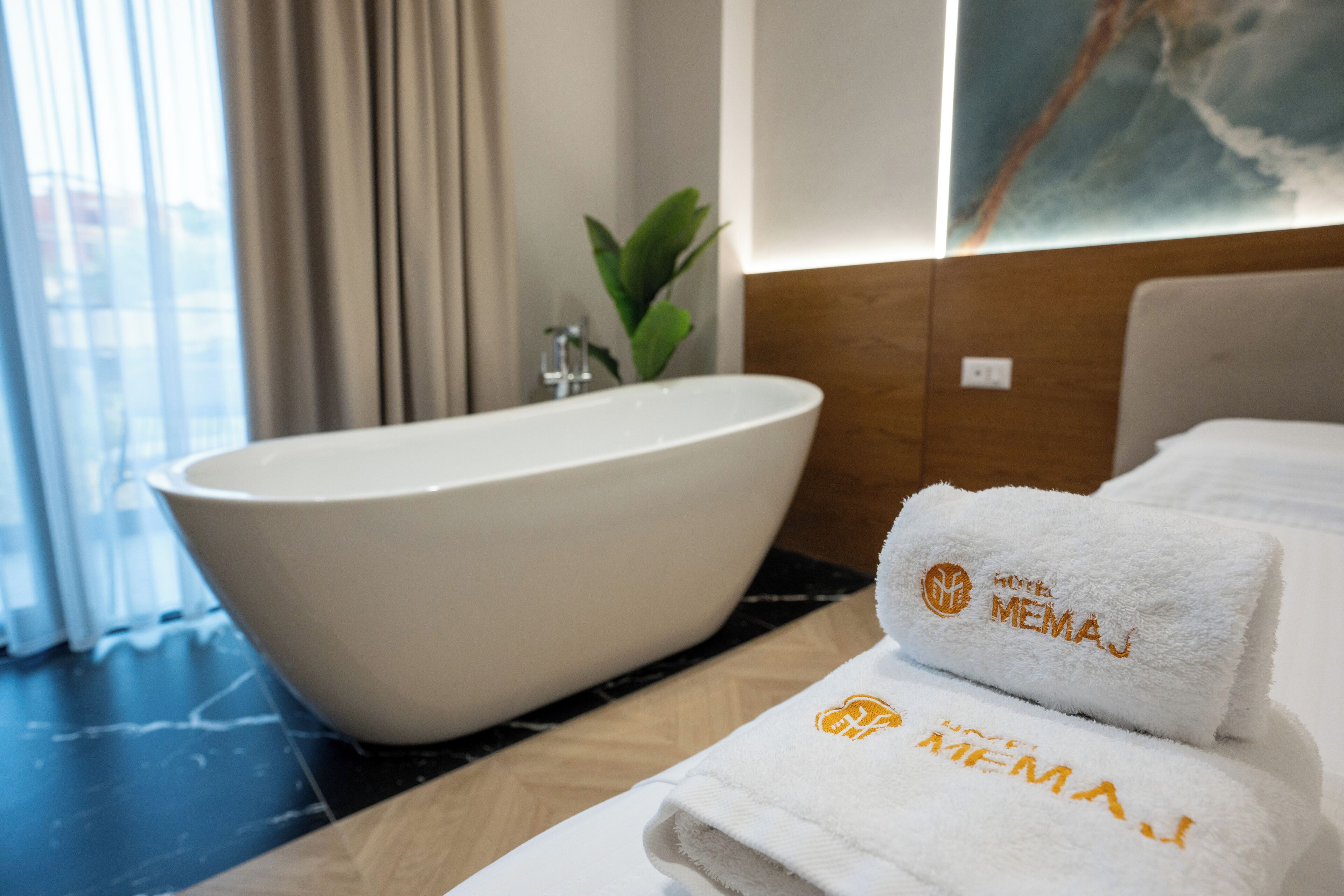 Un baño moderno con una bañera independiente, una planta y toallas dobladas con un logotipo.