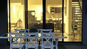 An outdoor patio with a table and chairs, a covered area with a ceiling, and a view into a modern interior with a kitchen and dining area. -  Modern New Yorker Inspired Townhouse~ Full kitchen-Fast Wifi- Near Bunbury (Australind)