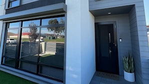 A modern two-story building with large windows, a flat roof, and a paved entrance area. -  Modern New Yorker Inspired Townhouse~ Full kitchen-Fast Wifi- Near Bunbury (Australind)