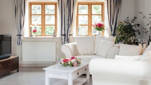 Ein Wohnzimmer mit einem weißen Sofa, einem Couchtisch und zwei mit Vorhängen versehenen Fenstern.