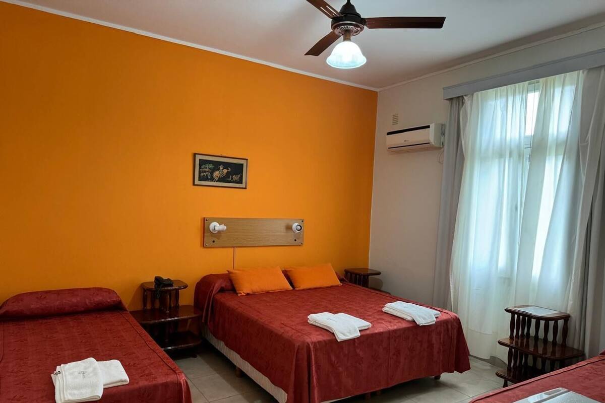 A hotel room with two beds, a ceiling fan, a window with curtains, and a small table.