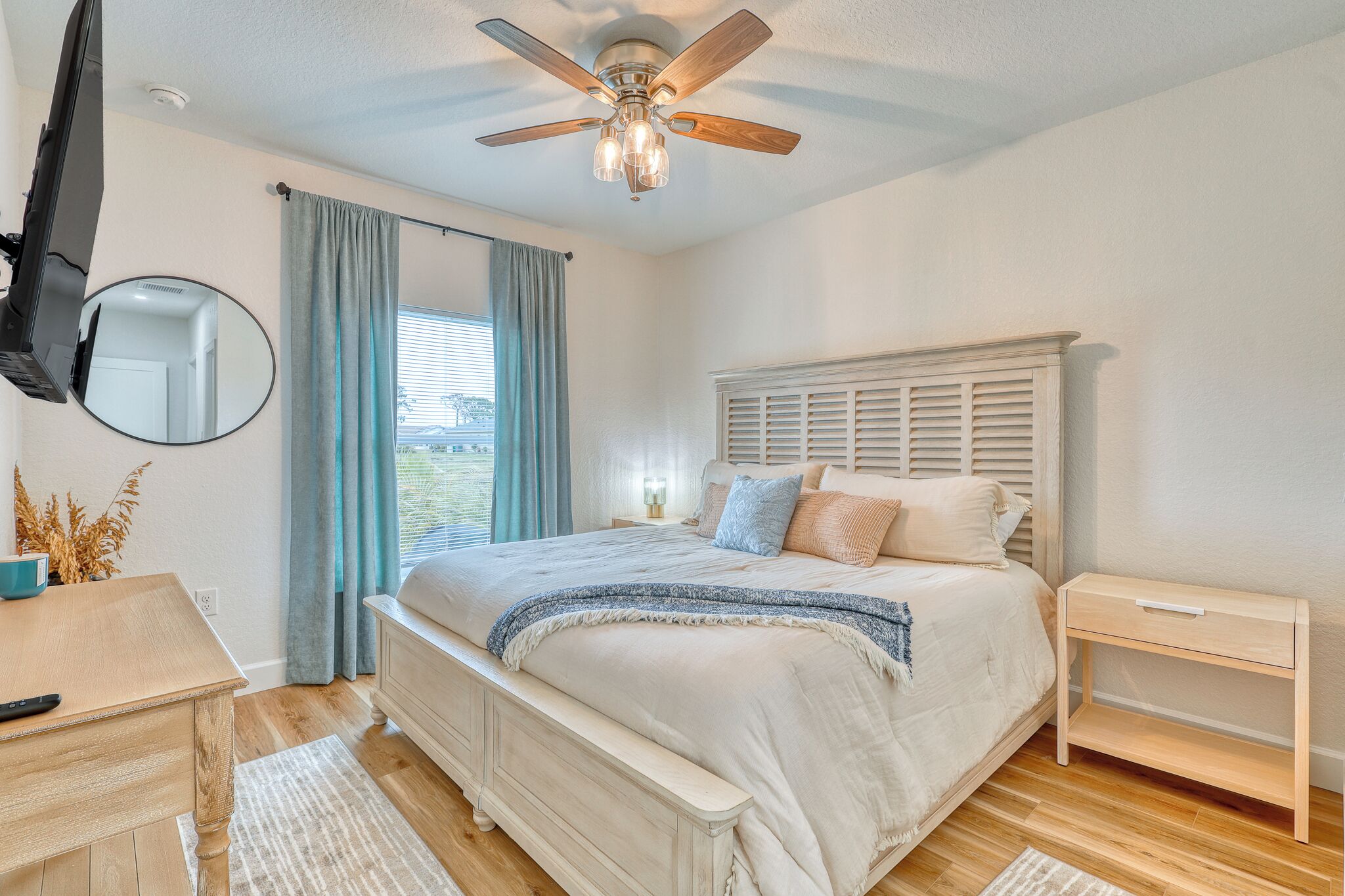 A bedroom with a bed, bedside table, nightstand, ceiling fan, and a TV mounted on the wall.