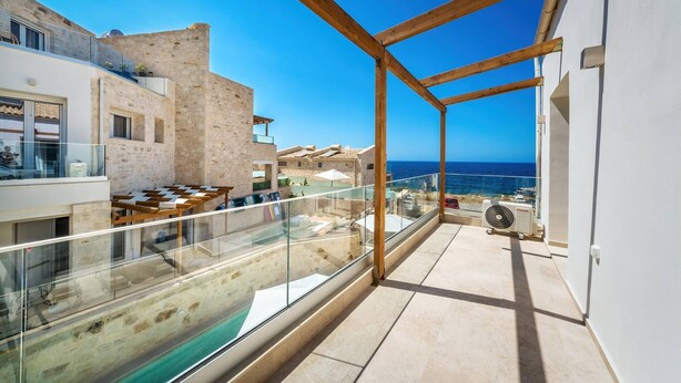Ein Balkon mit Glasgeländer, der auf einen Pool und einen wolkenlosen, blauen Himmel blickt.