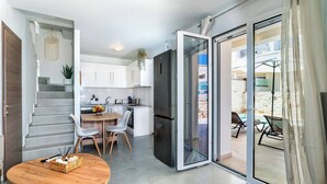 Eine moderne Küche mit weißen Schränken, eine Essecke mit einem Holztisch und Stühlen sowie eine Glastür, die auf eine Außenpatio führt.