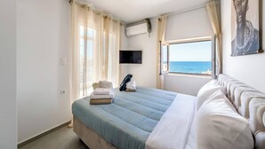 Ein Schlafzimmer mit Bett, Fernseher, Klimaanlage, Fenster mit Meerblick und einem Bild an der Wand.