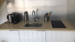 Una cucina con lavello in acciaio inossidabile, bollitore, macchina del caffè e portautensili.