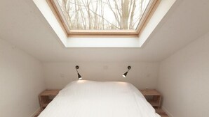 Une petite chambre à coucher, lumineuse, avec un puits de lumière, un lit et deux tables de chevet.