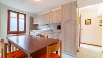 Una cocina moderna con armarios de madera, una mesa de comedor con cojines anaranjados y vistas al mar a través de una ventana.