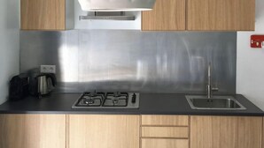 Une cuisine moderne avec des meubles en bois, un pare-feu en acier inoxydable, une cuisinière à gaz et un luminaire suspendu au design géométrique.