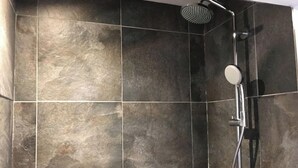 Un espace douche doté d’une pomme de douche à pluie et d’un pommeau de douche à main, de murs carrelés et d’un cadre de douche en métal.