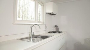 Une cuisine moderne avec un plan de travail blanc, un évier en acier inoxydable et une cuisinière à gaz.