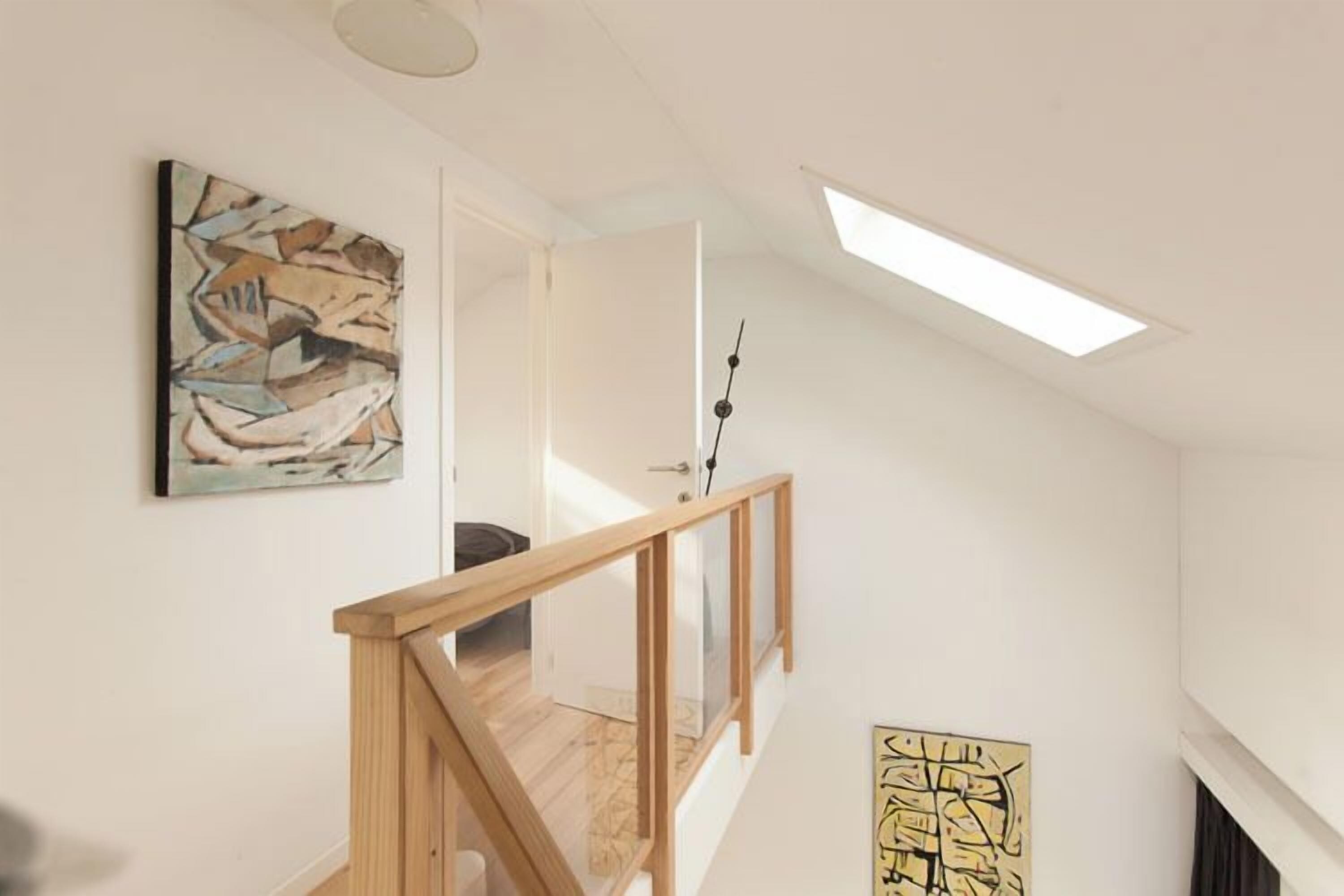 A modern interior with a wooden staircase, a skylight, and abstract art on the walls.