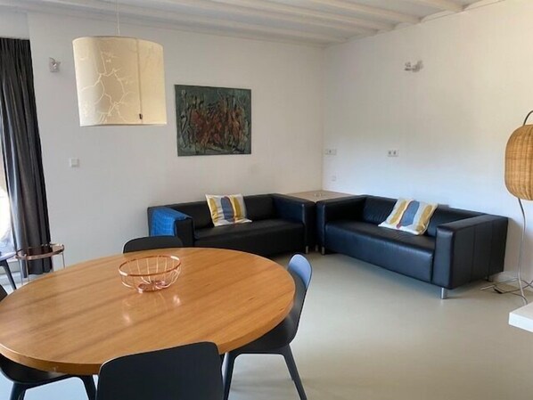 Una sala de estar moderna con una mesa redonda de madera, sofás negros y un cuadro en la pared.