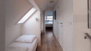 Un estrecho pasillo con tragaluz, una cama y una puerta que da a otra habitación.
