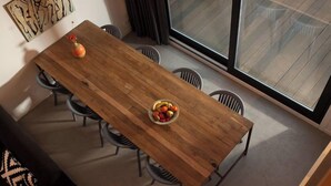 Un comedor con una mesa de madera, sillas, un frutero y un jarrón.
