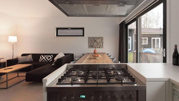Una cocina moderna con una isla central, una mesa de comedor y un sofá en una sala de estar luminosa con ventanas amplias.