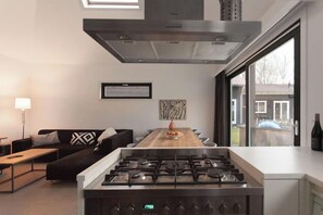 Une cuisine moderne avec un îlot central, une table à manger et un canapé dans un espace de vie lumineux doté de grandes fenêtres.